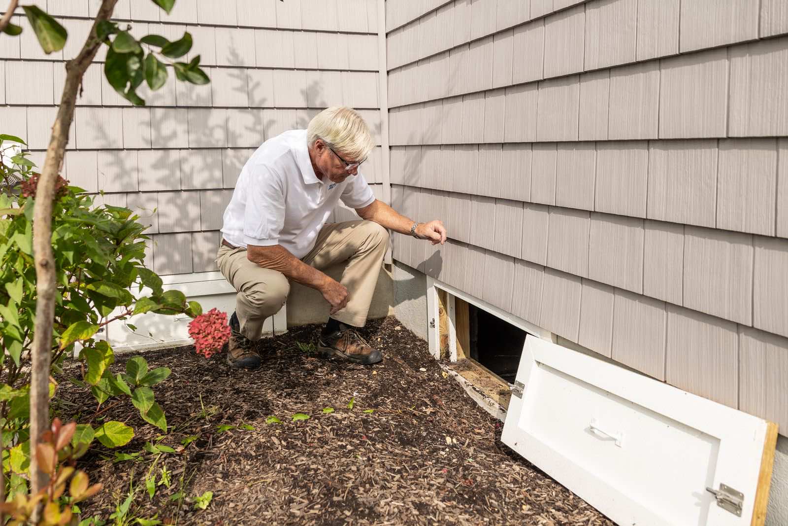 Inspector opening a crawl space access hatch at the base of a house