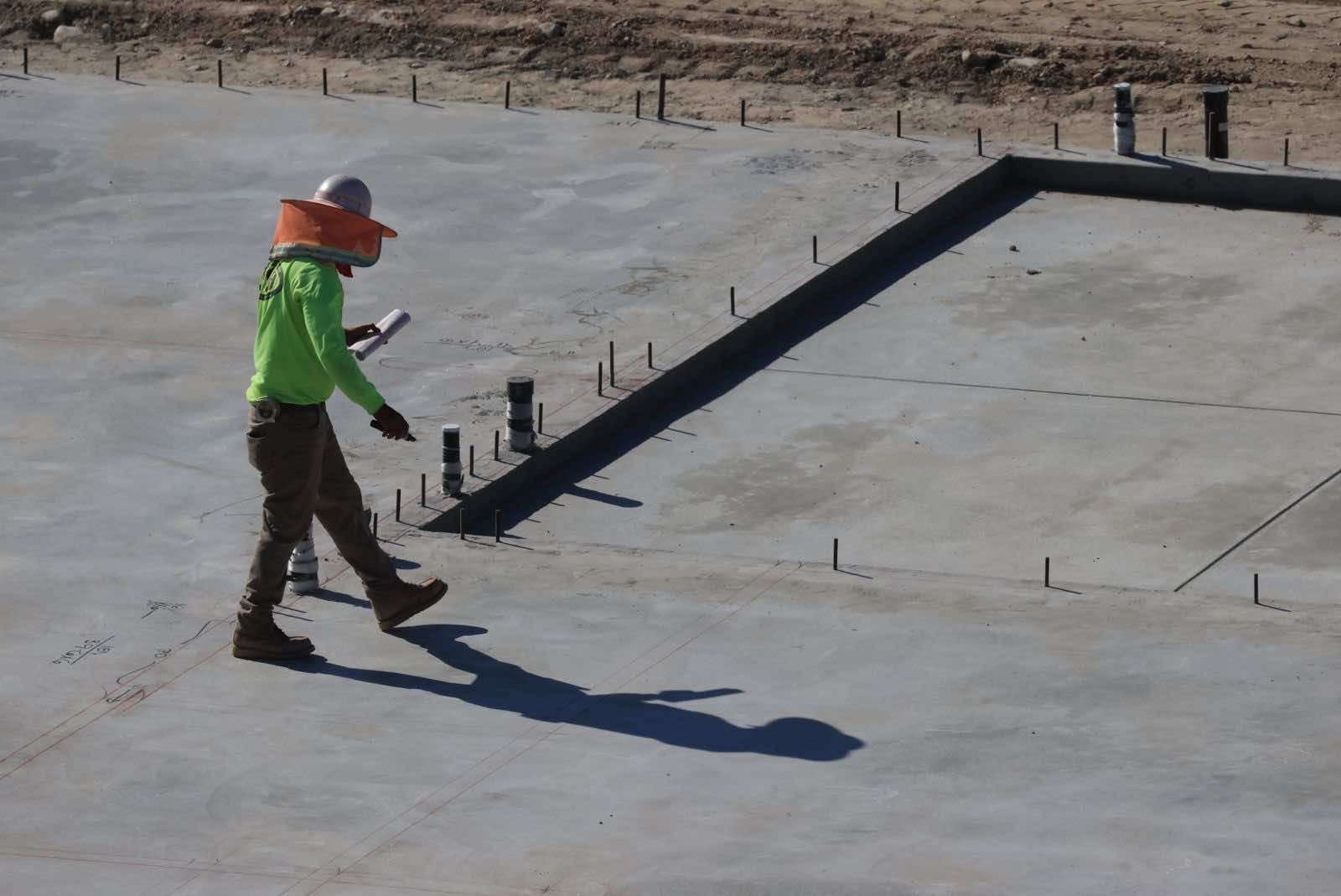 Worker on a newly poured concrete slab foundation with grade beam and rebar