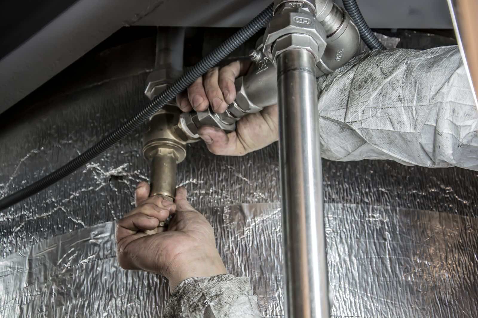 Plumber working on supply piping beneath a floor